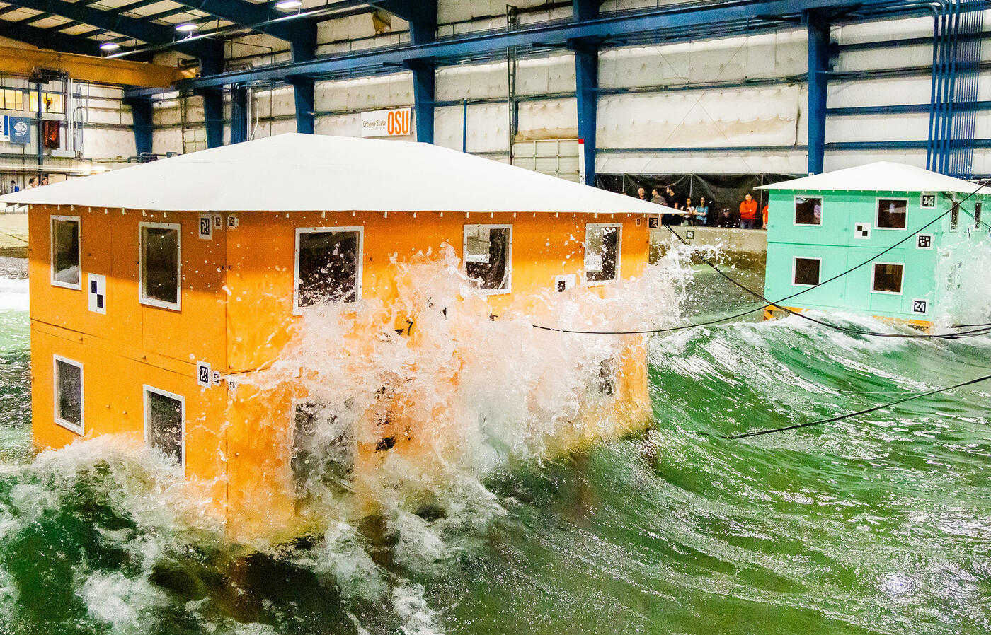Waves crash into model buildings. Testing at the O.H. Hinsdale Wave Research Laboratory may help inform future building design in coastal communities.