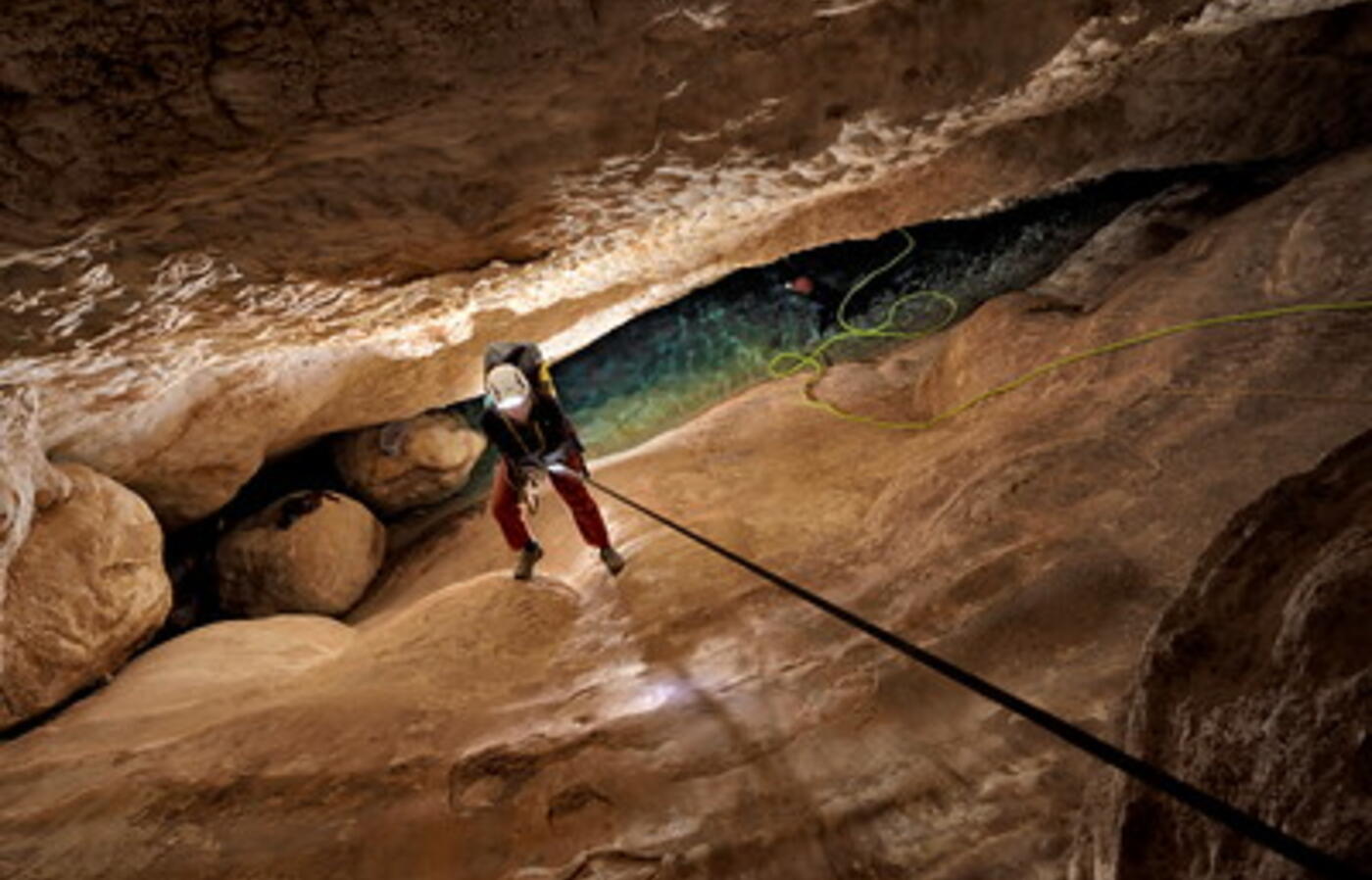 A researcher descends into a deep and narrow cave on a rope