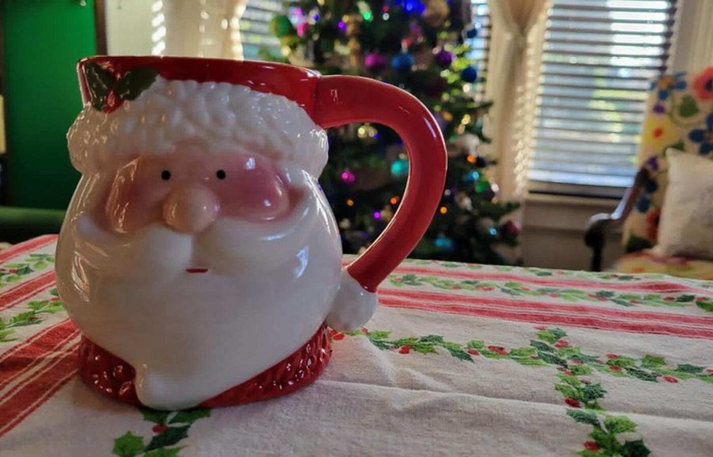 Coffee mug in the shape of Santa's head and face, with a white beard and red handle. 
