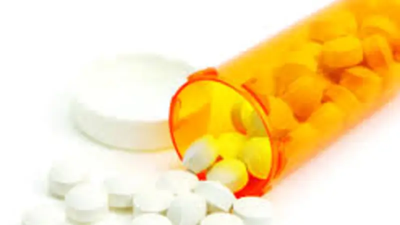 Stock image of an orange plastic bottle of white pills spilling out.