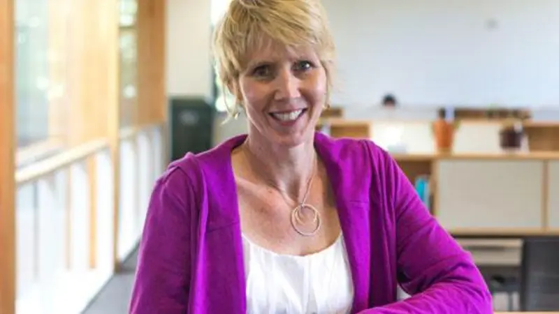 A woman smiles as she poses for a photo in an office environment.