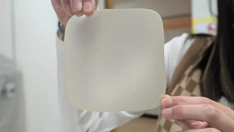 Student holding thin sheet of packaging material made of spent coffee grounds.