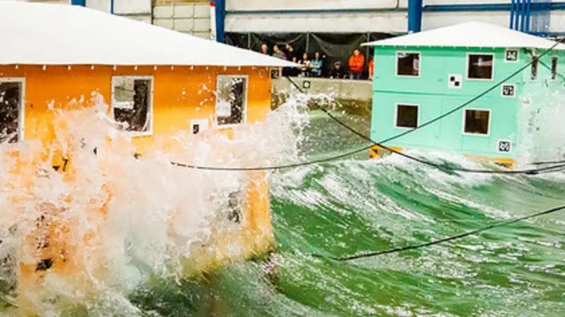 Waves crash into model buildings. Testing at the O.H. Hinsdale Wave Research Laboratory may help inform future building design in coastal communities.