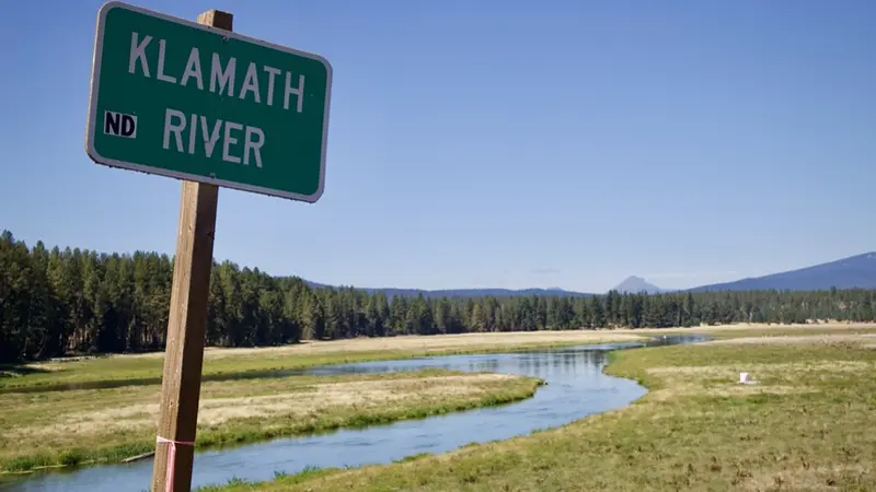Sign saying Klamath River next to the river with trees in background