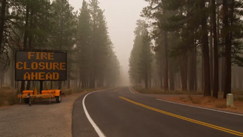 Image of sign indicating road closure due to forest fire with smoke heavy in the air.