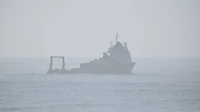 A vessel sits in the ocean, visible through hazy skies. 