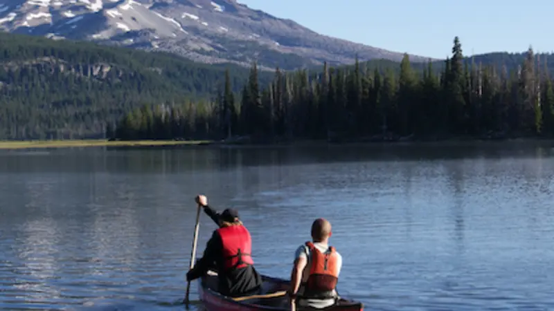 Stock image of two people paddling a canoe on a river with a mountain in the background