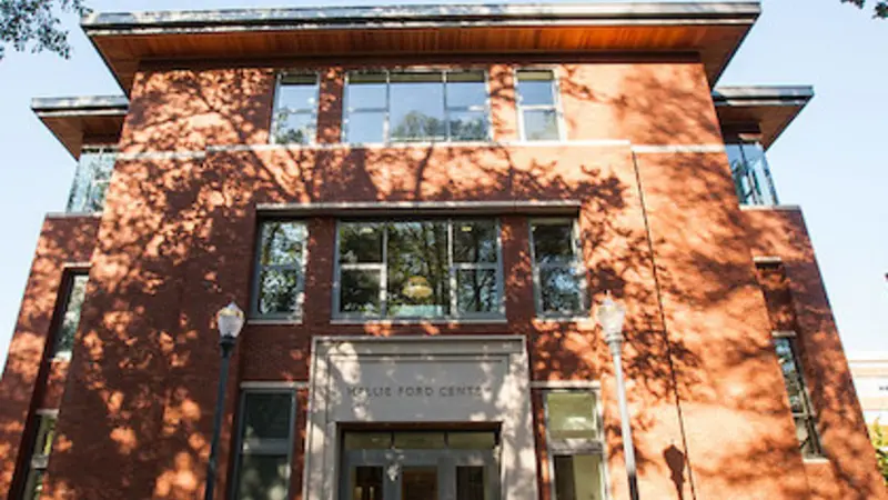 Image of the front of the Hallie E. Ford Center, looking up, as bright sunlight filters through the trees.