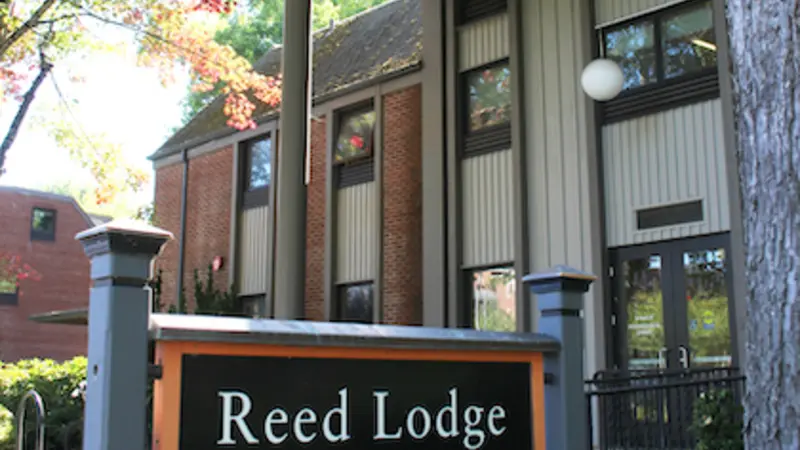 Image shows Reed Lodge on OSU campus, with an orange-and-black sign in the foreground bearing its name.