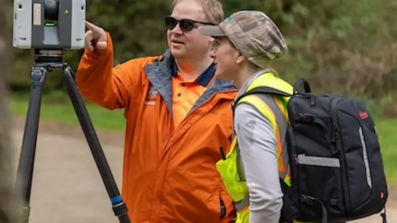 Image shows Prof. Mike Olsen with graduate student Dana Lind wearing a bright yellow safety vest as they look at a scanner perched on a tripod.