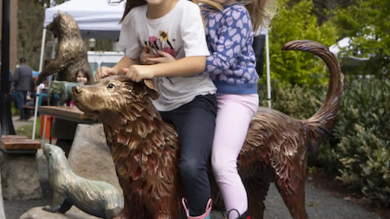 Two children laughing atop the lifesize bronze sculpture of a dog outside OSU's veterinary college at Pet Day 2022.
