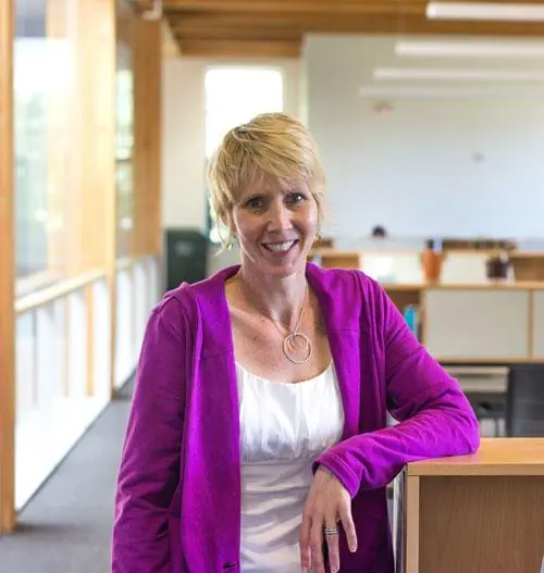 A woman smiles as she poses for a photo in an office environment.