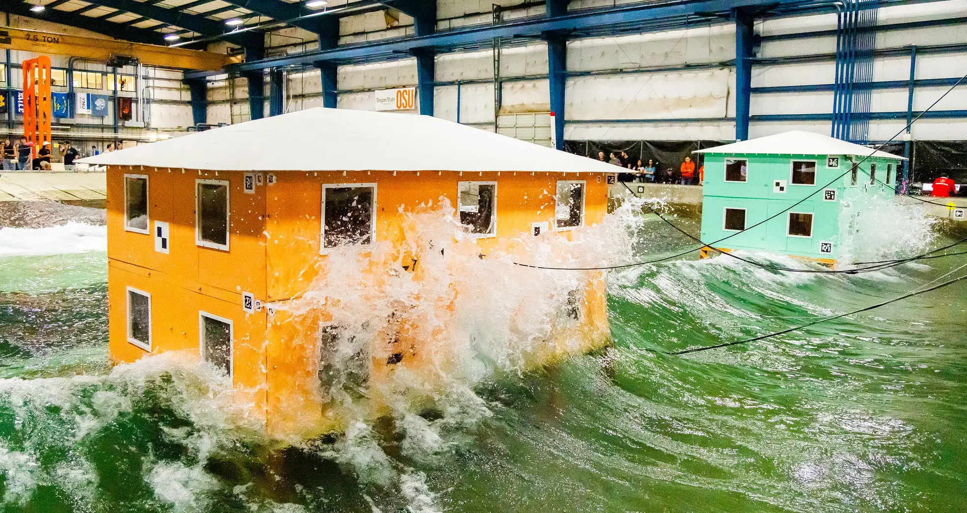 Waves crash into model buildings. Testing at the O.H. Hinsdale Wave Research Laboratory may help inform future building design in coastal communities.