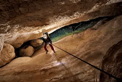 A researcher descends into a deep and narrow cave on a rope