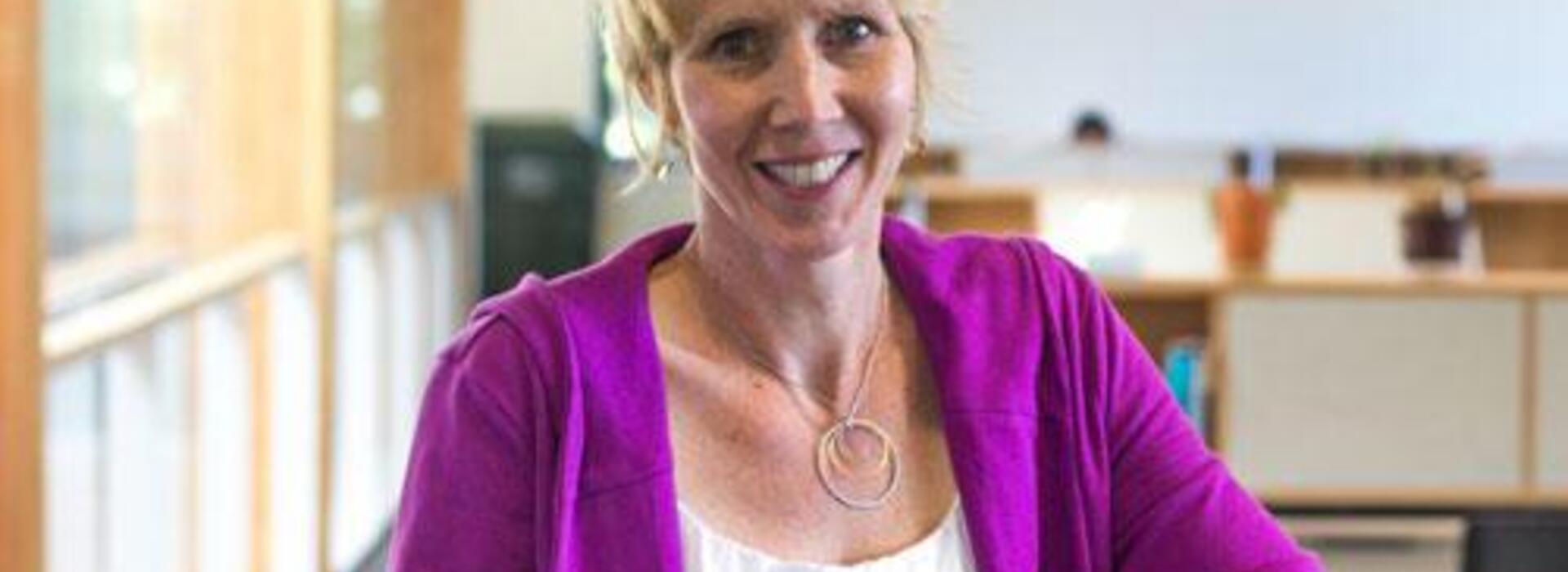 A woman smiles as she poses for a photo in an office environment.