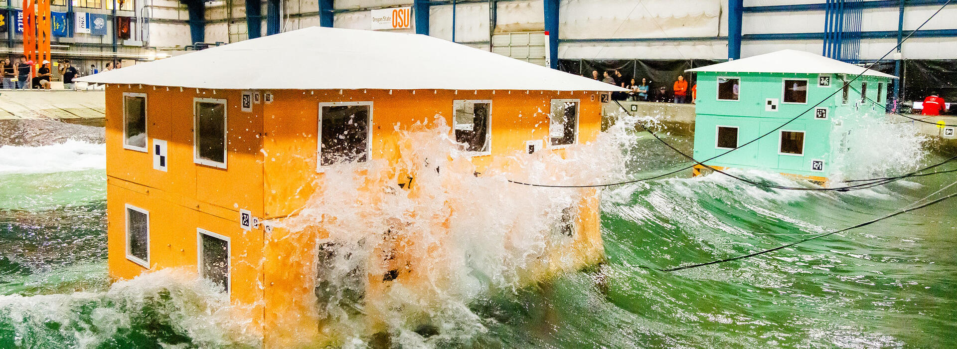 Waves crash into model buildings. Testing at the O.H. Hinsdale Wave Research Laboratory may help inform future building design in coastal communities.