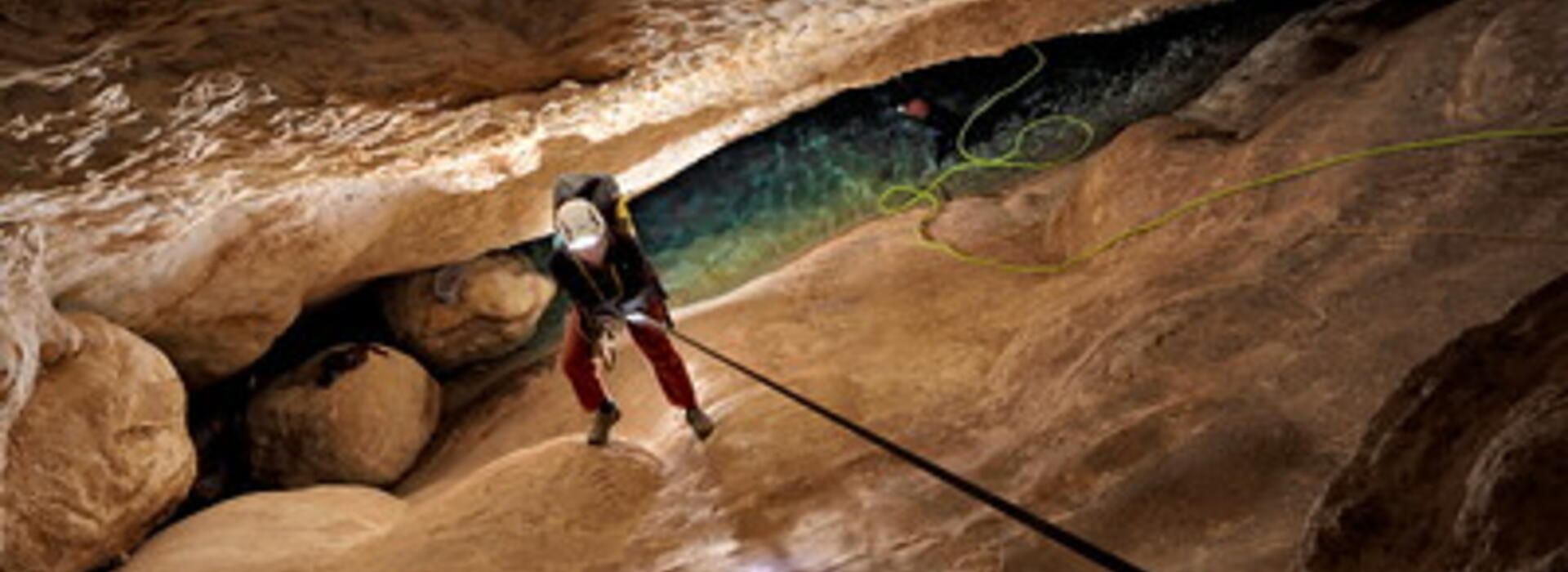 A researcher descends into a deep and narrow cave on a rope