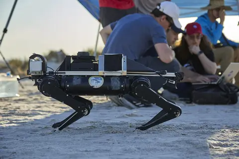 Quadruped robot on and with researchers in background huddled around a computer