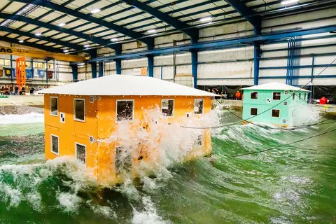 Waves crash into model buildings. Testing at the O.H. Hinsdale Wave Research Laboratory may help inform future building design in coastal communities.
