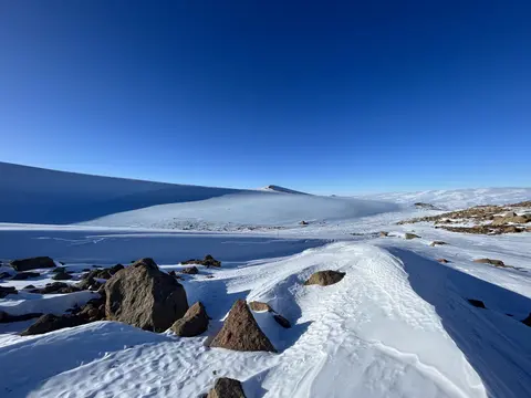 Snowfield with rocks in the foreground and bright blue sky.