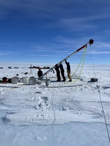 Researchers lift an ice core drill into place on a snowfield. 